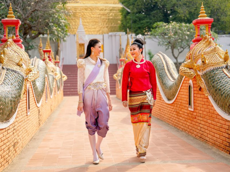 Thai women with traditional dress walk together and talk on walkway of famous temple